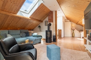 Una sala de estar estilo loft con techo alto, vigas de madera, chimenea, sofá, mesa de centro y televisor.