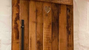 Een houten schuifdeur met een hartvormige uitsparing, een metalen handgreep en een zwarte rails erboven.