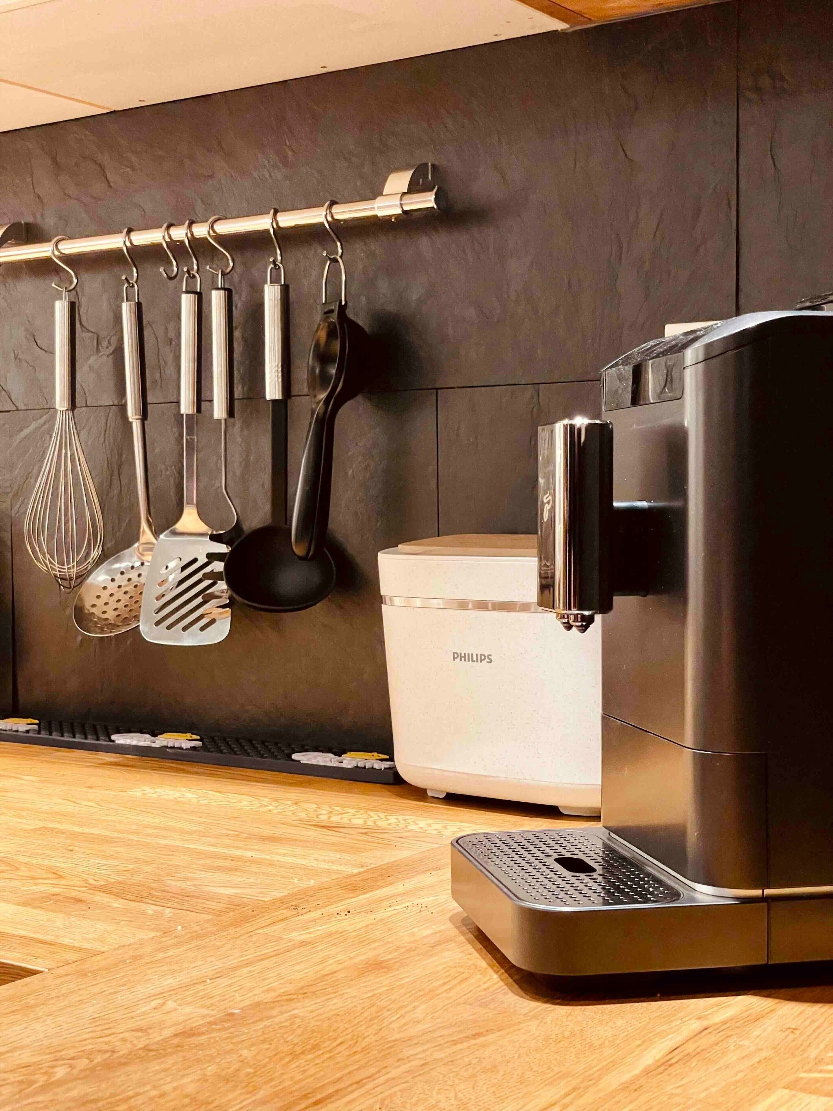 A kitchen with a coffee maker, a white container, and various utensils hanging on a rack.