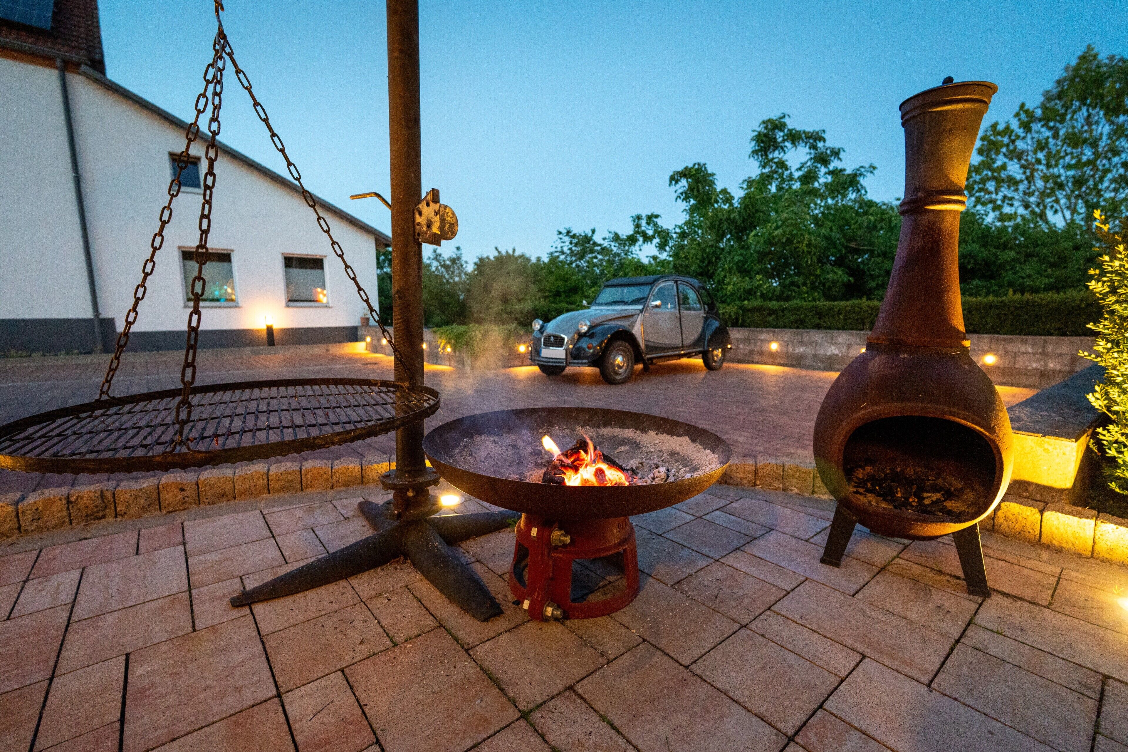 Eine Terrasse mit Feuerstelle, einer Hängetasche und einem Oldtimer im Hintergrund.