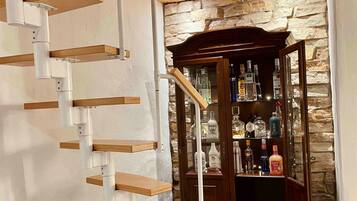 A spiral staircase with wooden steps and white railings, leading to a stone wall with a liquor cabinet.