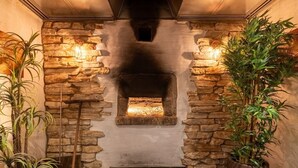 A stone fireplace with a fire, flanked by potted plants, and two wall-mounted lights. - Charming Eifel Bakehouse with Sauna, Private Terrace & EV Charging (Feuerscheid)