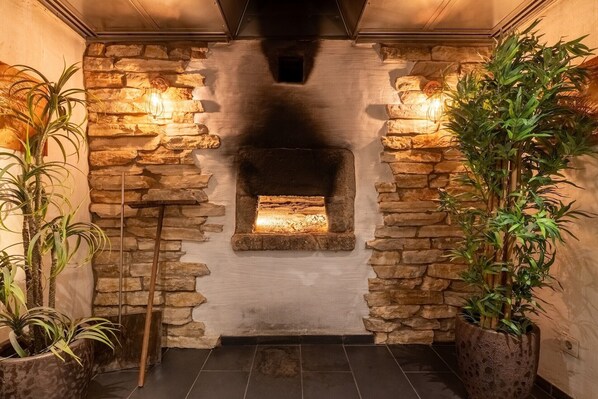 Una chimenea de piedra con fuego, flanqueada por macetas con plantas y dos luces fijadas en la pared.