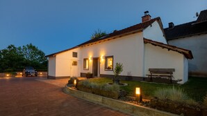 A white building with a tiled roof, a paved driveway, and a bench outside. - Charming Eifel Bakehouse with Sauna, Private Terrace & EV Charging (Feuerscheid)
