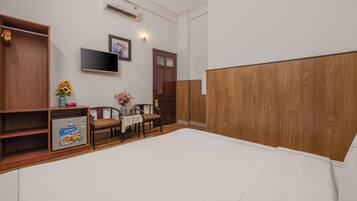 Quarto com uma cama grande, guarda-roupa de madeira, televisão na parede e uma pequena mesa com cadeiras.