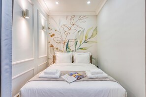 A hotel room with a bed, pillows, a magazine, and a wall with a leaf pattern.