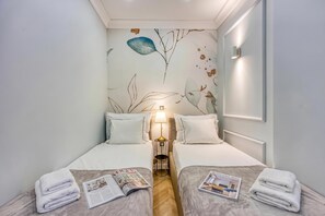 A hotel room with two beds, a nightstand, a lamp, and a magazine on the bed.