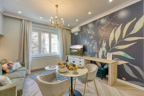 Ein modernes Wohnzimmer mit Essbereich, einer Kristallleuchter, einem Fernseher und einer Wand mit Blattmuster.