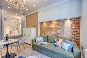 A modern living room with a green sofa, a dining area with a white table, and a brick accent wall.