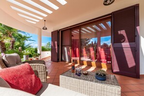 Eine sonnendurchflutete Terrasse mit Korbmöbeln, einer Flasche, Weingläsern und Topfpflanzen.
