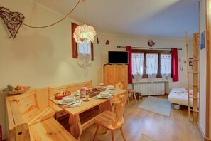 Une pièce chaleureuse avec une table à manger en bois, dressée pour deux personnes, un téléviseur et une fenêtre avec des rideaux.