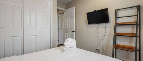 A neatly made bed with white linens, a television mounted on the wall, and a wooden ladder against the wall.