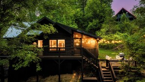 A log cabin with a wooden deck and stairs leading to a balcony, surrounded by trees. - New Hot Tub, Hammocks, Pet Friendly, Romantic Honeymoon Mountain Getaway (Pigeon Forge)