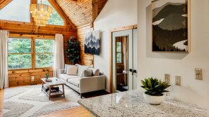 A cozy cabin interior with a wooden ceiling, a sofa, a coffee table, a potted plant, and a framed artwork on the wall. - New Hot Tub, Hammocks, Pet Friendly, Romantic Honeymoon Mountain Getaway (Pigeon Forge)