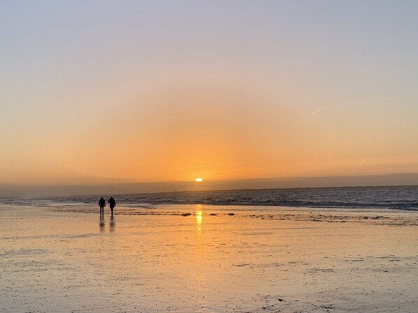 Una playa al atardecer con dos personas caminando sobre la arena.