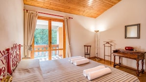 Une chambre d’hôtel avec un grand lit, un plafond en bois, un bureau avec des tiroirs, une lampe et une vue par la fenêtre.