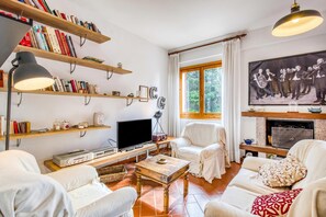 A living room with a fireplace, bookshelves, a television, and a large window. - Casa Acone In Mugello - Near Florence (Pontassieve)