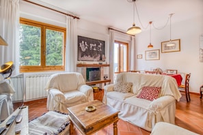 A living room with a fireplace, two white sofas, a wooden coffee table, and a dining area with a red tablecloth. - Casa Acone In Mugello - Near Florence (Pontassieve)