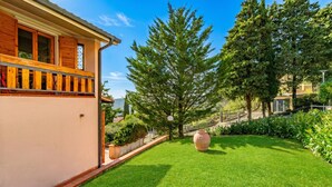 Une maison avec un balcon, une pelouse bien entretenue et de grands arbres.