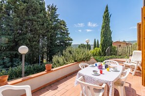 An outdoor patio with a table set for dining, surrounded by white chairs, potted plants, and a view of trees and a distant building. - Casa Acone In Mugello - Near Florence (Pontassieve)
