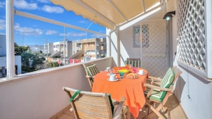 A balcony with a table set for two, chairs, and a view of buildings and greenery. - Bel Mare Apartment 200m from beach  (Melendugno)