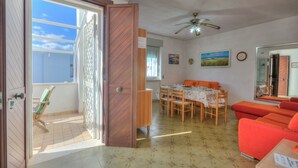 A dining area with a table and chairs, a red sofa, and a ceiling fan. - Bel Mare Apartment 200m from beach  (Melendugno)