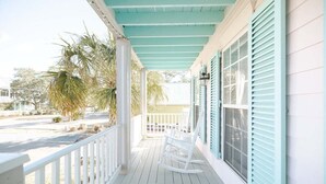 A porch with white railings and a teal ceiling, featuring rocking chairs and a view of the street. - New! Close to Beach w Hot Tub! (Carolina Beach)