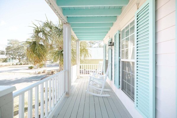 A porch with white railings and a teal ceiling, featuring rocking chairs and a view of the street.