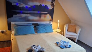 A bedroom with a bed, pillows, a chair, a nightstand, and a wall mural. - Urgemütliche Ferienwohnung, Offenes Spitzdach Nähe Weinanbaugebieten (Salmtal)