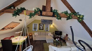 A cozy attic room with a wooden ceiling, a sofa, a dining table, and a TV. - Urgemütliche Ferienwohnung, Offenes Spitzdach Nähe Weinanbaugebieten (Salmtal)