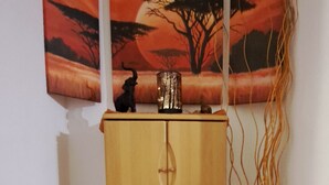 A corner with a wooden cabinet, a vase with long reeds, and a three-panel painting of a tree and sunset. - Urgemütliche Ferienwohnung, Offenes Spitzdach Nähe Weinanbaugebieten (Salmtal)