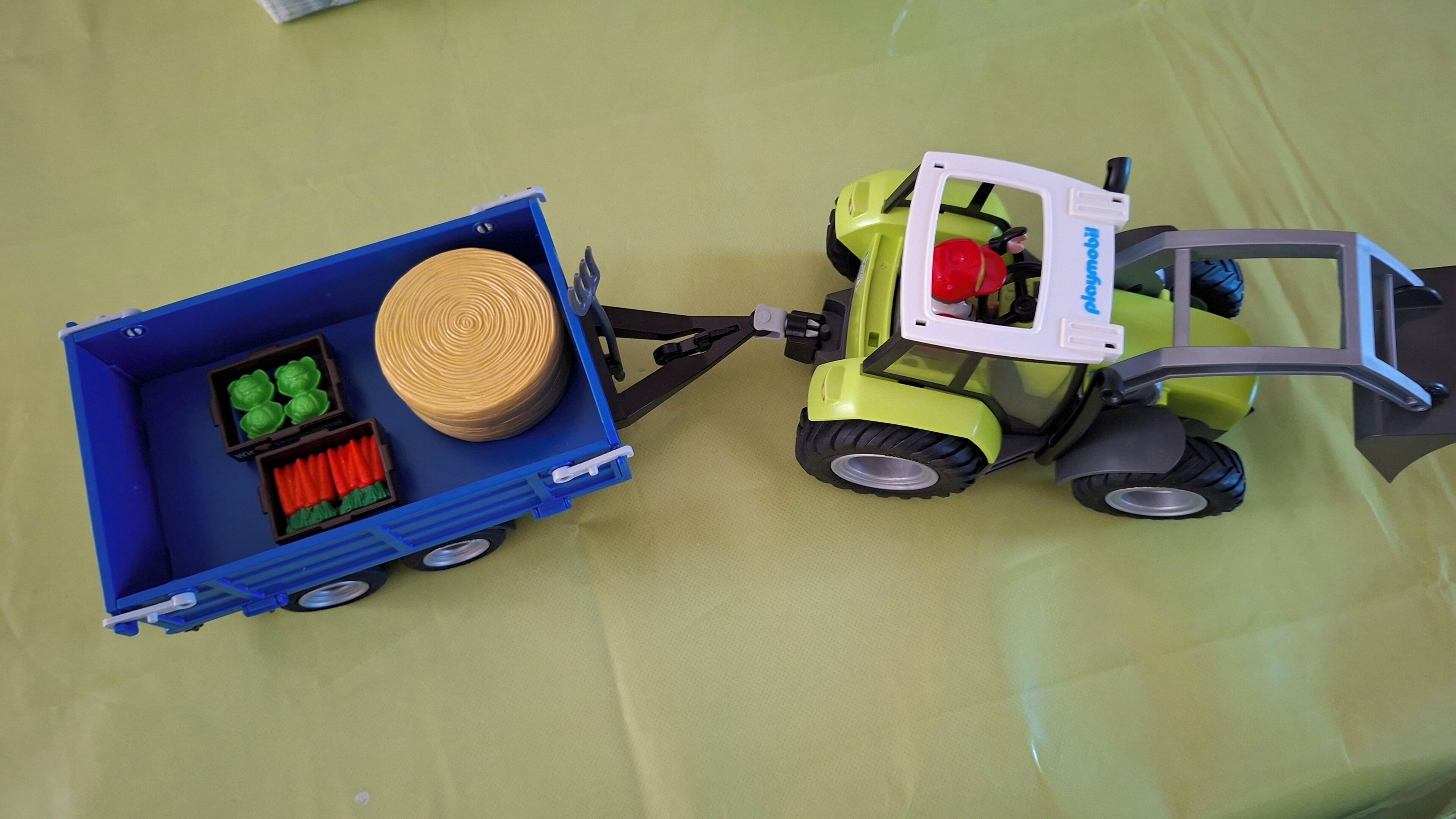 A toy forklift with a blue trailer attached, containing a spool of yellow rope and green and red objects.