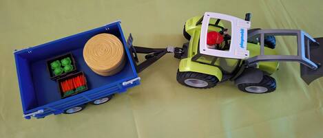A toy forklift with a blue trailer attached, containing a spool of yellow rope and green and red objects.
