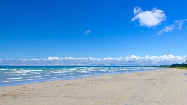 Une vaste plage de sable fin, avec des vagues douces et un ciel bleu dégagé.
