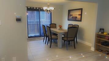 A dining area with a table and chairs, a chandelier, a window with curtains, and a shelf with items.