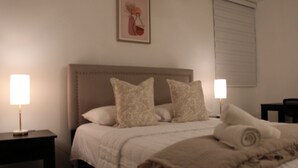 Ein ordentlich bezogenes Bett mit Kopfteil, zwei Nachttischlampen und einem gerahmten Bild an der Wand.