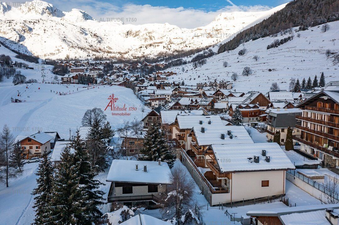 A snow-covered mountain village with traditional wooden buildings, a ski slope, and a clear view of the surrounding mountains.