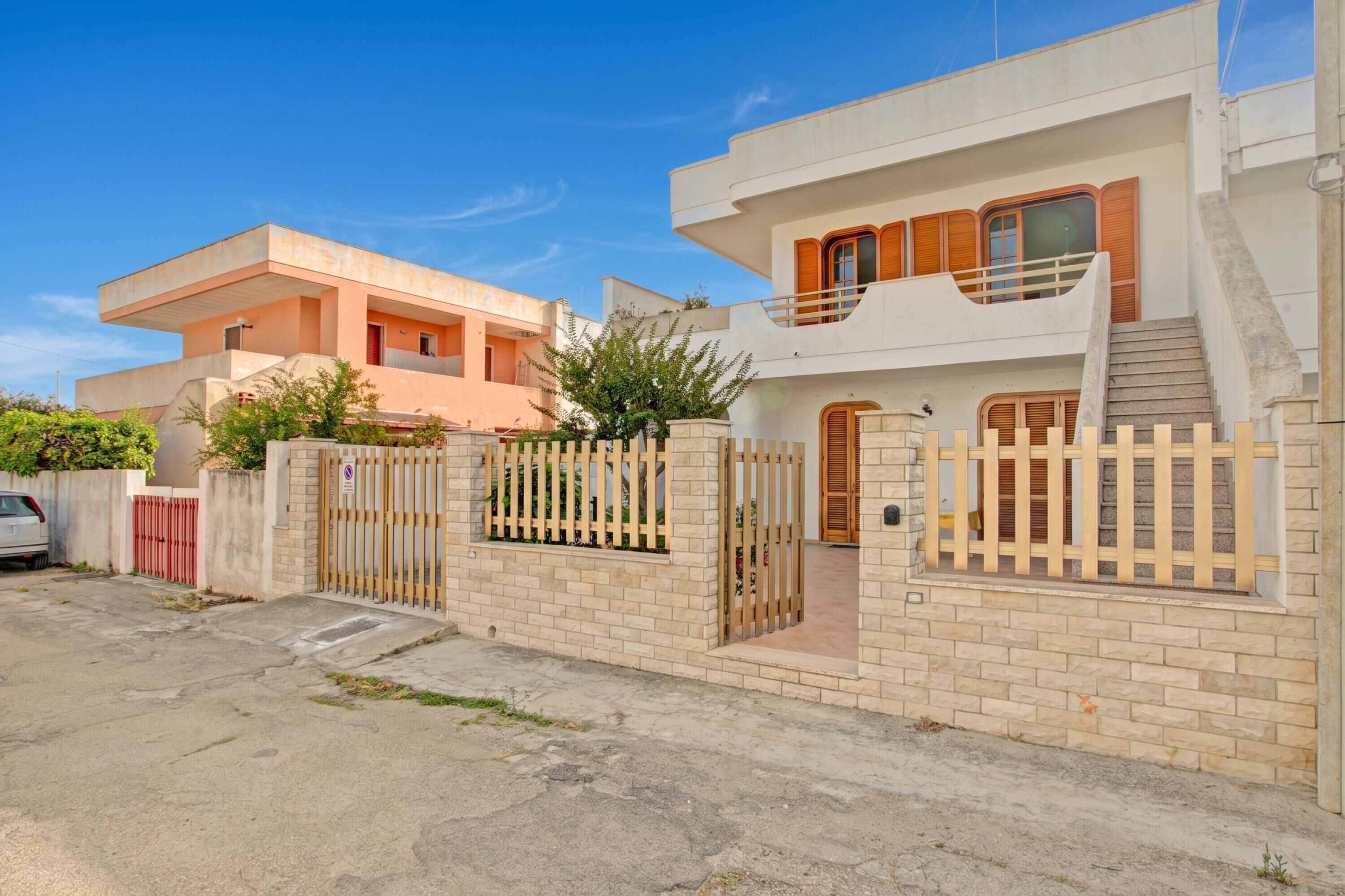A modern two-story house with a gated entrance, a staircase, and a balcony.