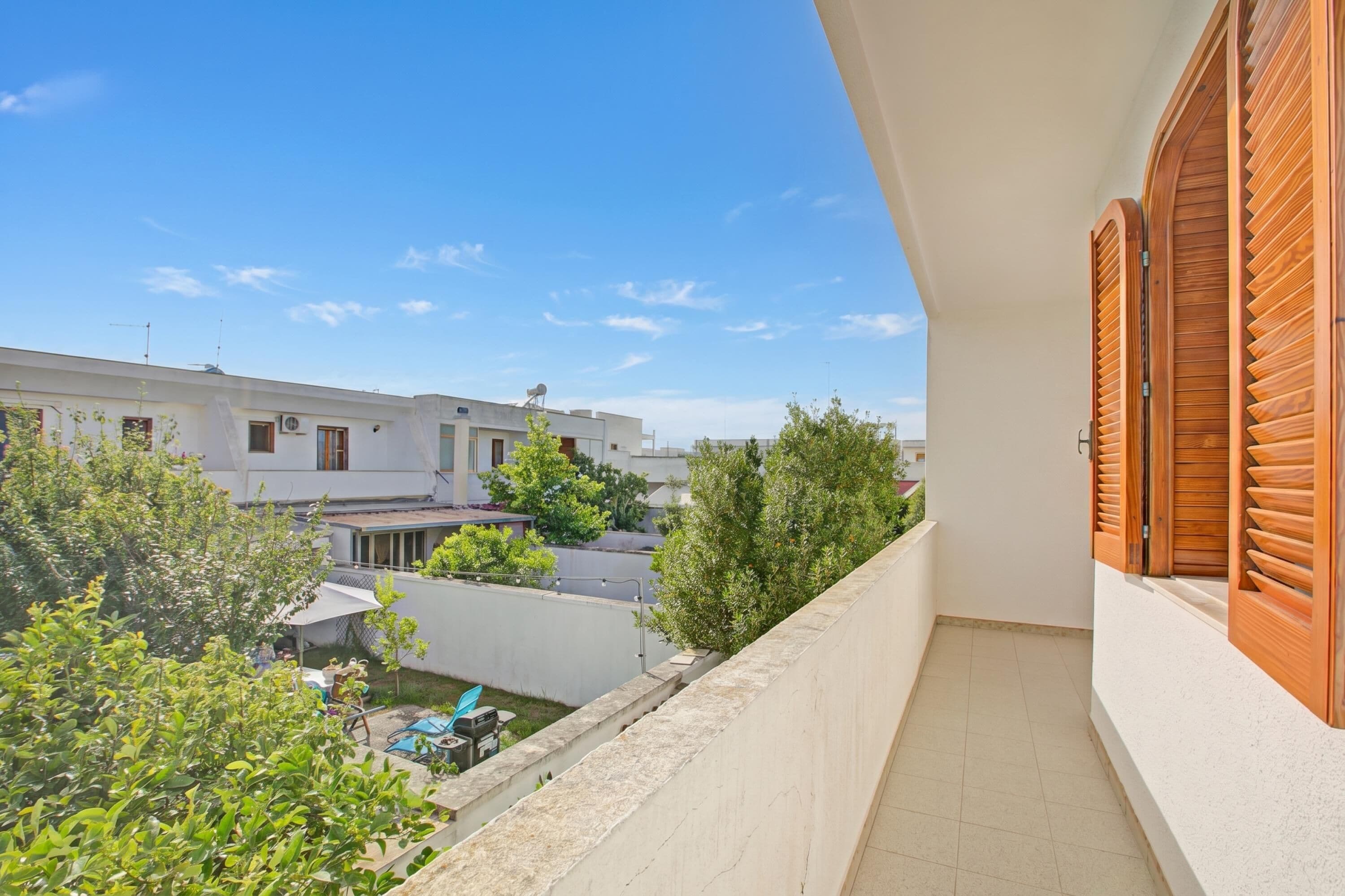 A balcony with a view of a residential area, a white building with a flat roof, and a clear blue sky.