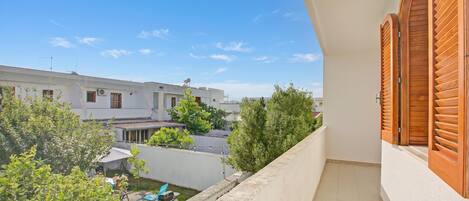 A balcony with a view of a residential area, a white building with a flat roof, and a clear blue sky.