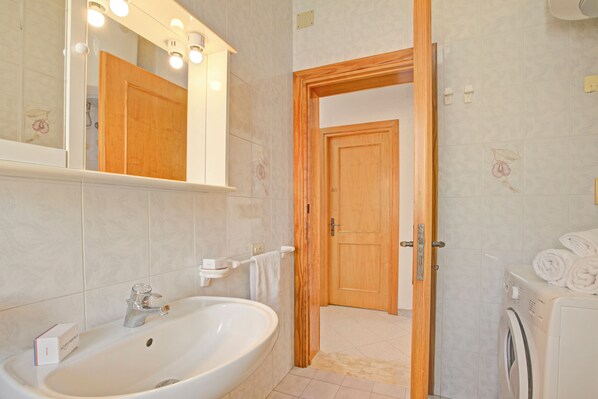Un baño con lavamanos, espejo y puerta de madera que da a otra habitación.