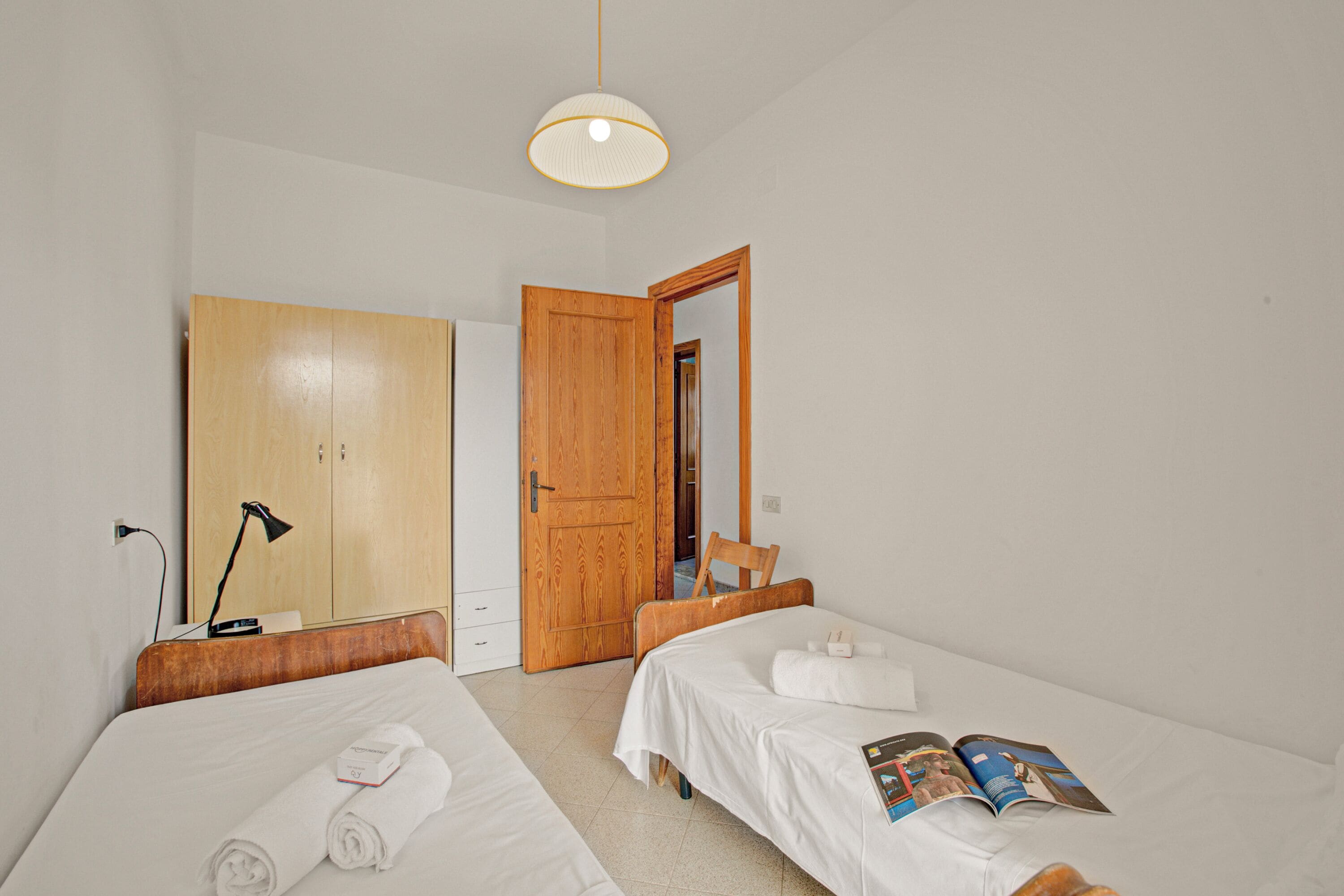A hotel room with two beds, a wooden wardrobe, a desk, and a chair.