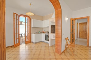 Een keuken met witte kastjes, een fornuis en een eethoek met een tafel en stoelen.