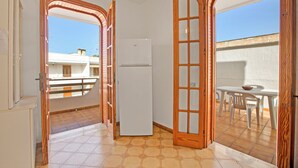 A room with a white refrigerator, a dining table with chairs, and a view of a building outside. - Casa Marangi 250 meters from the sea (Melendugno)