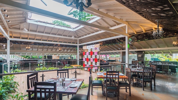 Un espace de restauration intérieur avec des tables et des chaises en bois, un mur décoratif agrémenté de compositions florales et une vue sur la verdure à l’extérieur.