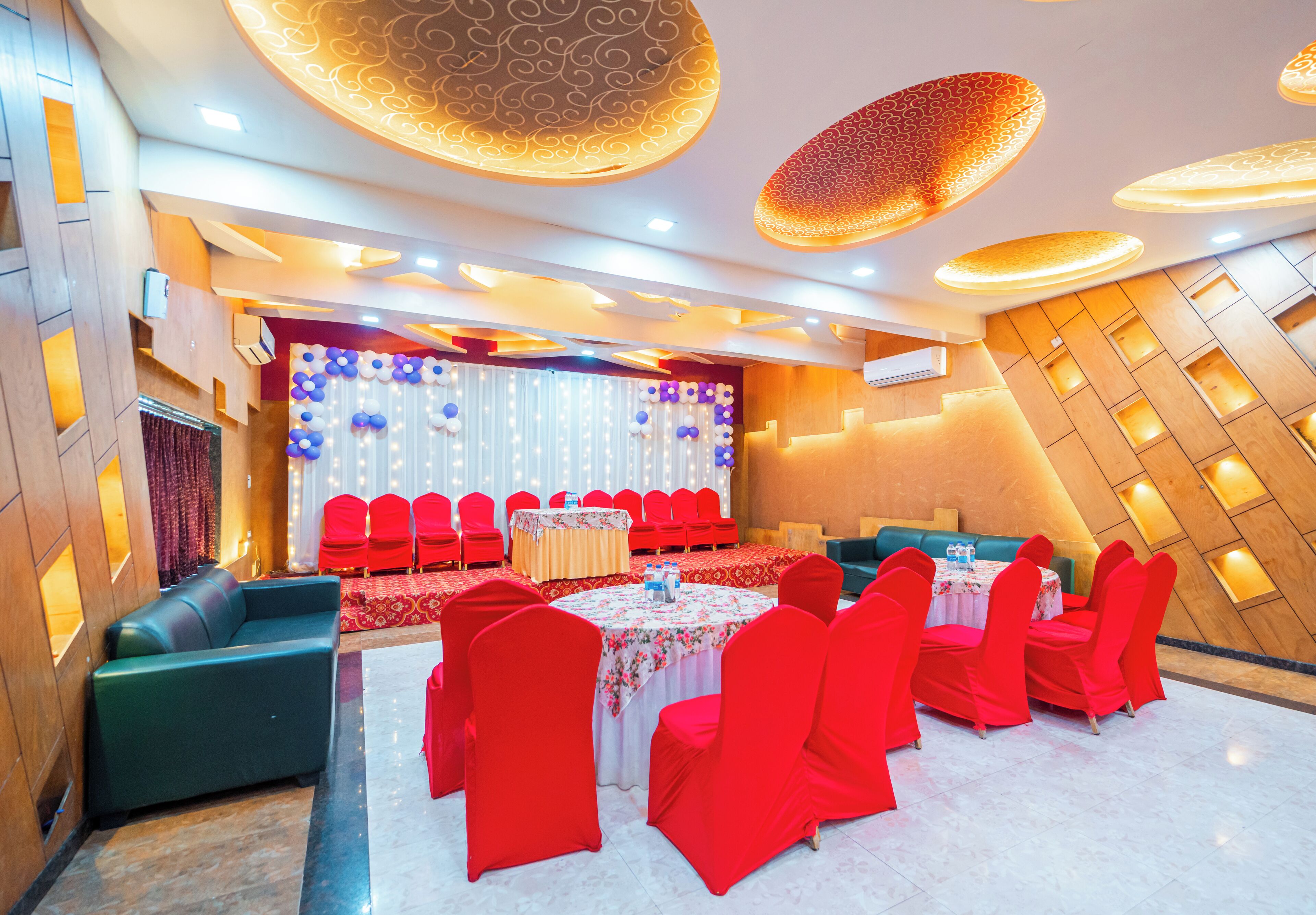 A banquet hall with round tables, red chairs, and a stage with a curtain backdrop.
