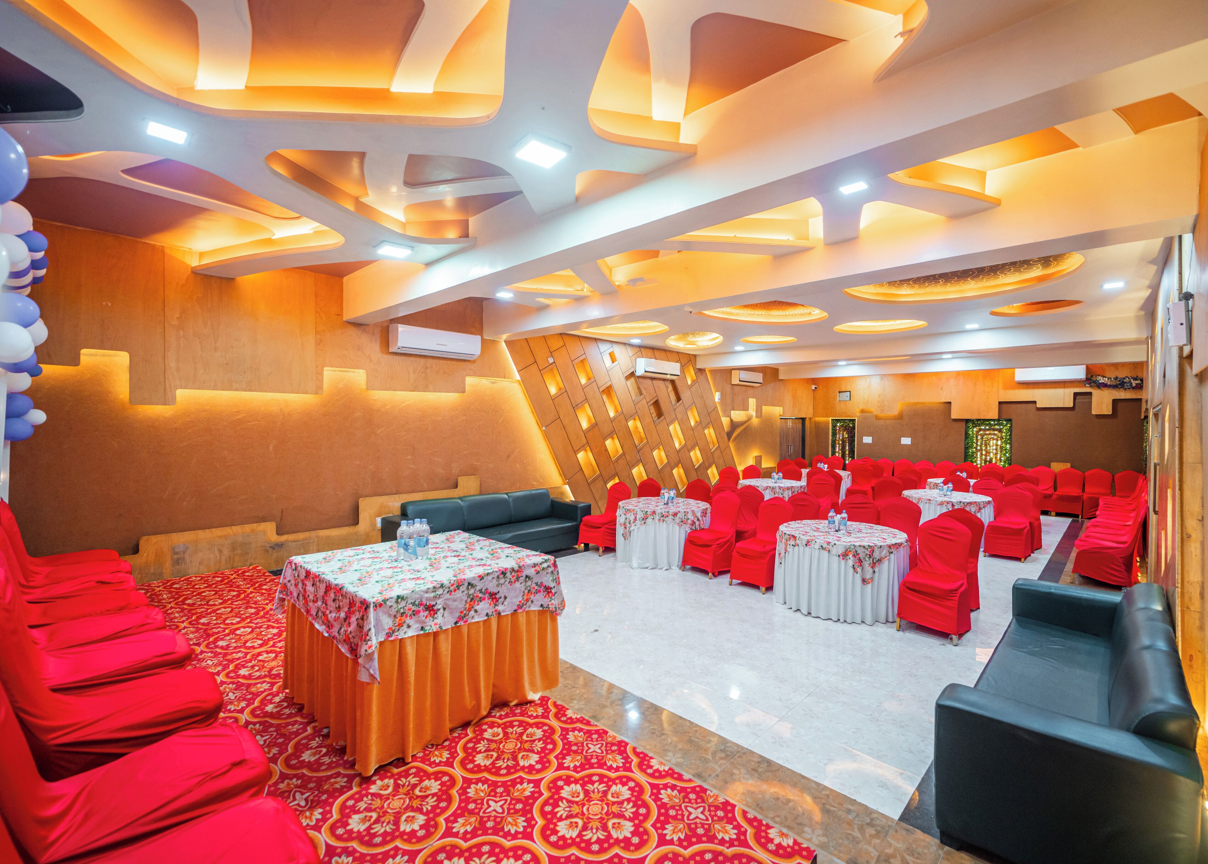 A banquet hall with red chairs and tables, a patterned carpet, and a modern ceiling design.