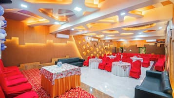 A banquet hall with red chairs and tables, a patterned carpet, and a modern ceiling design.