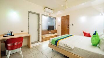 A hotel room with a bed, a desk with a chair, a wardrobe, and a mirror.