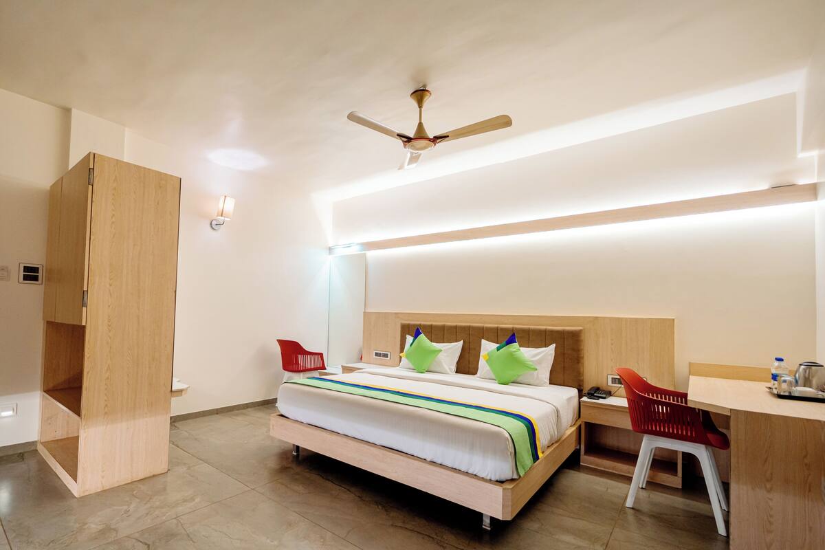 A modern hotel room with a wooden bed, a desk, a chair, and a ceiling fan.